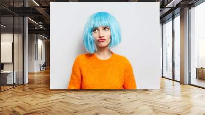 Portrait of cute girl with blue  hair in orange sweater looking up against white background. Wall mural