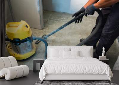 The builder cleans the floor from dust with a construction vacuum cleaner. Wall mural