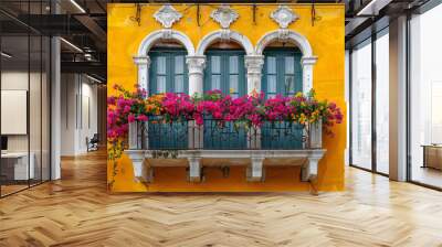 a yellow building with a green door and a balcony adorned with red flowers and green plants. Wall mural