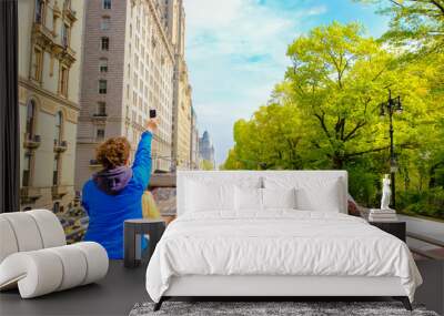 Tourists enjoying views of New York City from top of open roof bus in spring; woman in blue is taking photos with her smartphone Wall mural