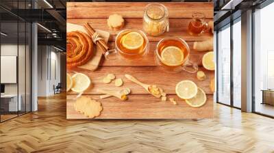 Cup of tea with lemon, honey, ginger root ingredients and sweet cinnamon bun on wooden table. Natural medicine concept. Mockup for your design. Top view. Wall mural