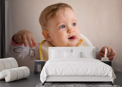 One-year-old girl with her tongue out and a bib in a high chair. Wall mural