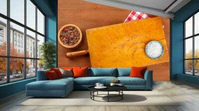 A photo of a wooden chopping board, shot from the top on a dark rustic texture with salt, pepper, a vichy cloth, and a place for text. A gastronomy background with copy space Wall mural