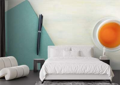 A top shot of a teal blue journal with a pen and a cup of tea, forming a frame on a light background with a place for text Wall mural