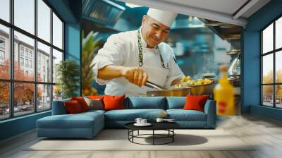 A chef in a white uniform and toque smiles as he prepares a meal in a professional kitchen. He is using tongs to stir vegetables in a pot on a stovetop. Wall mural