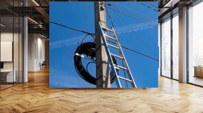 A metal staircase next to a concrete electric pole with a lot of wires against the blue sky. Preparation for electrical work. Wall mural