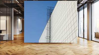 Long metal staircase on the gray modern facade of an industrial building, warehouse or shopping center against the blue sky. Symbol of the stairway to heaven Wall mural