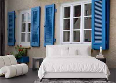 Two windows with white wooden frames, blue shutters and decorative flower boxes. Image of trendy decor, comfort, beautification. Wall mural