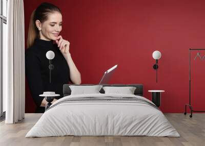 Portrait of a beautiful smiling caucasian woman working on tablet isolated on a red background Wall mural