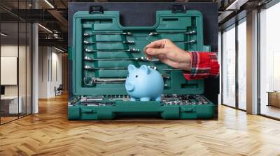 A female hand puts a coin into a blue piggy bank against the background of an open box with a tool. The concept of saving money for a gift to a man Wall mural