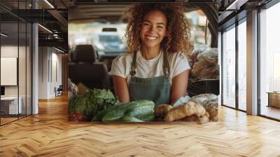 A cheerful female vendor stands behind a truck laden with fresh vegetables and goods, radiating positive energy and friendliness in a market setting under daylight. Wall mural