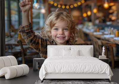 A cheerful young boy raising his arm in a victory pose at a café, with a bright smile and casual attire Wall mural