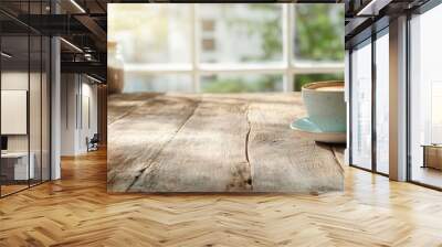 A cup of coffee in a speckled blue mug sits on a wooden table near a window, surrounded by plants, with sunlight streaming through, creating a serene morning mood. Wall mural