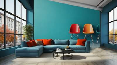 A lineup of colorful chairs – red, orange, and teal – positioned against a teal wall, creating a vibrant and contemporary design concept in a minimalist setting. Wall mural