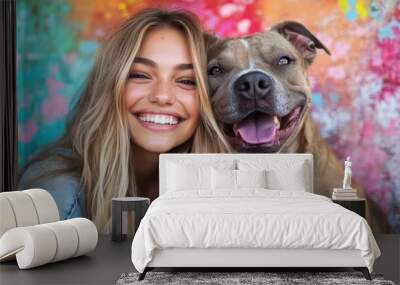 A smiling blonde woman with long hair poses happily with her brown dog in front of a lively, abstract wall filled with vibrant colors and patterns. Wall mural