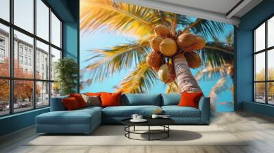 A tropical mood captured with vibrant coconuts clustered at the top of a palm tree against a clear blue sky Wall mural