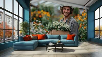 Smiling young man with curly hair holding a crate of white flowers in a greenhouse garden Wall mural