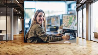 Smiling woman working with dual monitors displaying maps Wall mural