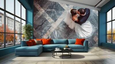 A bride and groom are dancing in a large room with a marble floor. The bride is wearing a white dress and the groom is wearing a blue suit. The couple is smiling and enjoying their time together Wall mural