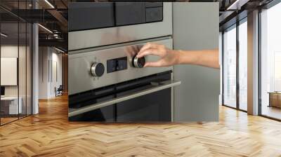 A hand adjusts a knob on a modern stainless steel oven, likely setting the temperature or cooking mode Wall mural