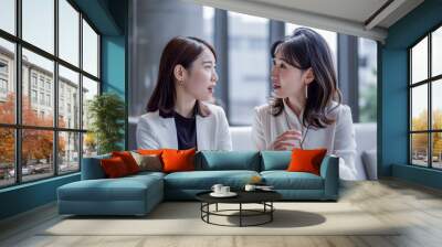 women are sitting at a table, talking to each other. One of them is wearing a white shirt and the other is wearing a black shirt. They are both looking at each other, engaged in conversation Wall mural