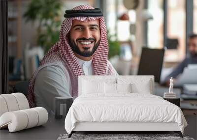  smiling man wearing a red and white scarf sits in front of a computer. He is smiling and he is happy Wall mural