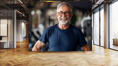 man with a big smile on his face is posing in a gym. He is wearing a blue shirt and has his arms crossed. The gym is filled with various equipment, including a few dumbbells and a bench Wall mural