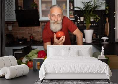 Picture of mature handsome bearded man standing at the kitchen and cooking salad Wall mural