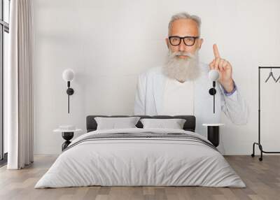 Portrait of old cheerful man in glasses pointing up with finger and looking camera over white wall Wall mural