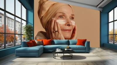 Senior woman is applying makeup to her face. She is smiling and looking at the camera. Concept of self-care and confidence Wall mural