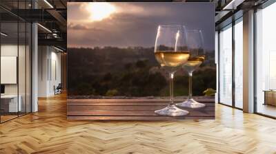 Two elegant glasses of white wine on a table with countryside in the background, at sunset Wall mural