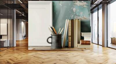 A desk featuring a white picture frame and pencils in an iron mug set on top of books and a wooden box. Display concept. Wall mural