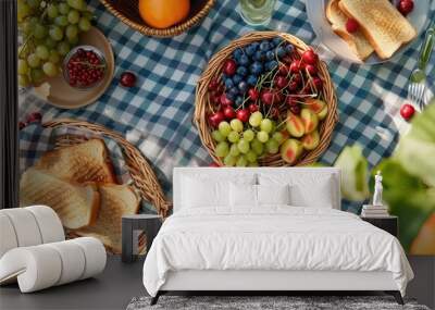 Aerial view of a summer picnic on a picnic blanket with a basket of fruits, toasted sandwiches, and berries, on a tablecloth. Wall mural