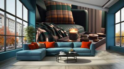 Modern living room hygge decor for fall. Interior design components in dark green, plush pillows, a plaid sofa with a chocolate muffin, an aroma drink cup on a wood tray, and a burning scented candle Wall mural