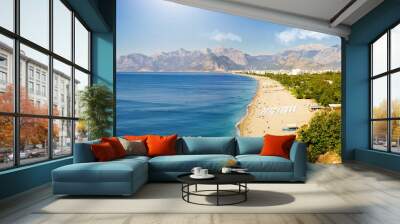 Amazingly beautiful panorama of Mediterranean resort Antalya: turquoise sea, white surf line, clean wide beach, greenery of parks, chain of mountains on horizon with clouds, sun and bright blue sky. Wall mural