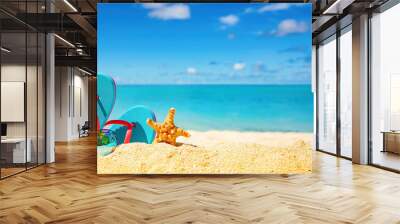 Beautiful colorful background for summer beach holiday. Sunglasses, starfish, turquoise flip-flops on sandy tropical beach against blue sky with clouds on bright sunny day. Wall mural