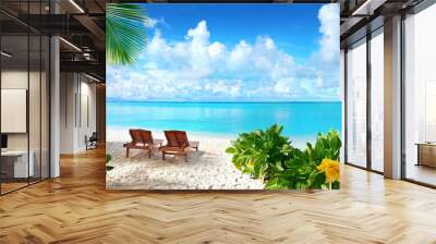 Beautiful tropical beach with white sand and two sun loungers on background of turquoise ocean and blue sky with clouds. Frame of palm leaves and flowers. Perfect landscape for relaxing vacation. Wall mural