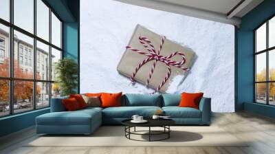 Brown paper package tied up in candy cane striped string buried in snow Wall mural