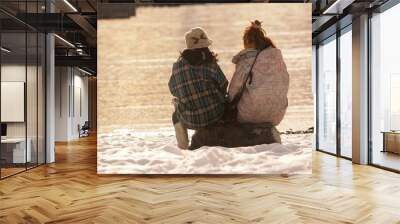 two ladies sitting in the snow by a lake Wall mural