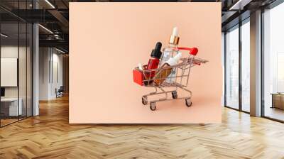 Online shopping minimalistic concept. Small cart with cosmetic bottles. Essential oil, serum and peeling gel in glass droppers. Mixture of beauty products. Black Friday Sales Wall mural