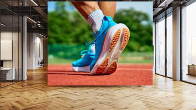 Athlete wearing bright blue running shoes on red stadium track during training. Sportsman legs in sport sneakers at racetrack. Fitness and healthy lifestyle concept Wall mural