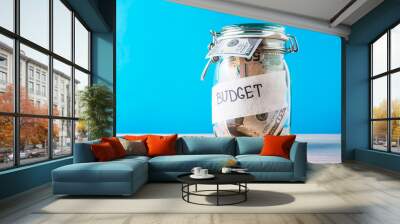 Finance and investment concept. Glass saving bank with dollar bills and inscription budget on a blue background Wall mural