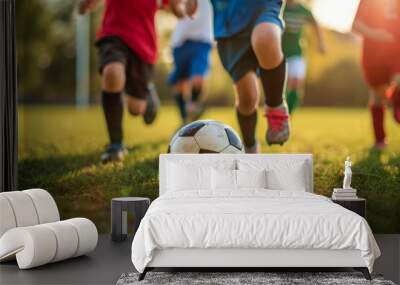 Football training for children. Group of young kids play soccer, running fervently after ball on the lush green grass under the warm glow of the afternoon sun Wall mural