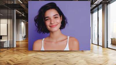 Portrait of beautiful young woman with short dark hair in white tank top smiling on purple background Wall mural