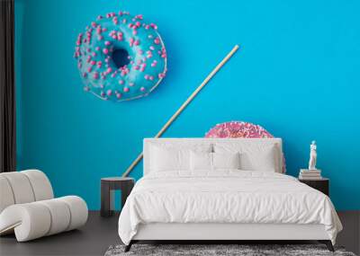 Two donuts separated with a drinking straw on blue background. Creative food concept Wall mural