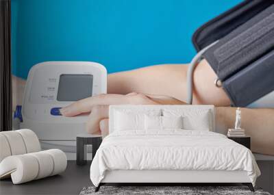 Woman measuring blood pressure with a digital pressure monitor against blue background. Health care and medical concept Wall mural