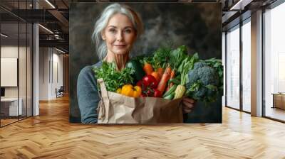 Studio portrait of a confident, middle-aged vegan woman holding a paper bag of fresh vegetables against a brown background Wall mural