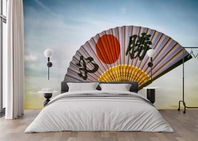 Hand of Japanese sports supporter holding a fan decorated with kanji characters spelling out hissho (English translation: certain victory) at sunrise Wall mural