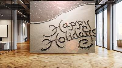 Happy Holidays message handwritten in smooth sand with an oncoming wave in the lens flare of the tropical sun Wall mural