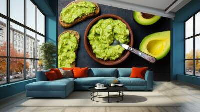 Traditional latinamerican mexican sauce guacamole in clay bowl and avocado sandwiches on dark background. Top view Wall mural